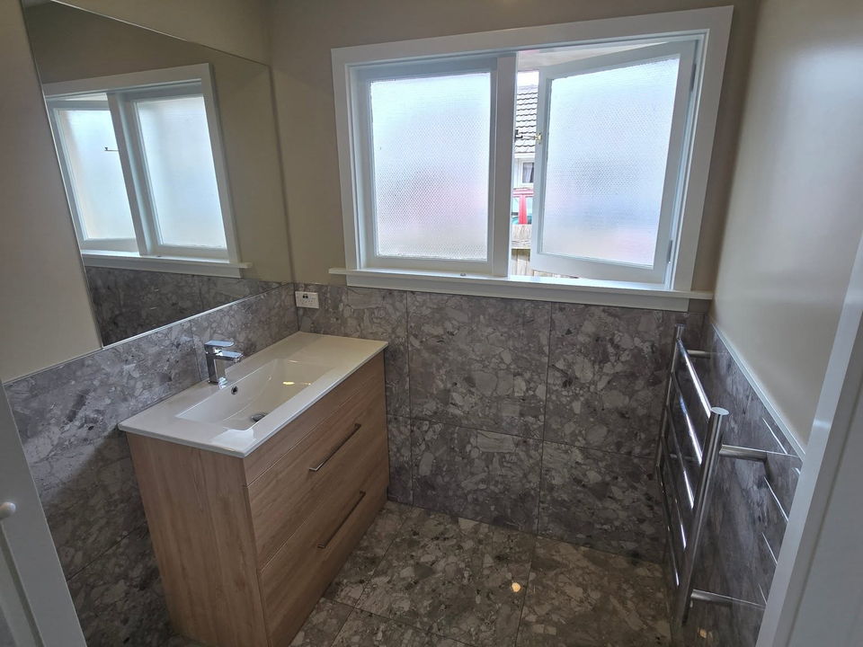 After: the same bathroom with a wall-hung timber-look vanity, grey stone-look tiles and a heated towel rail