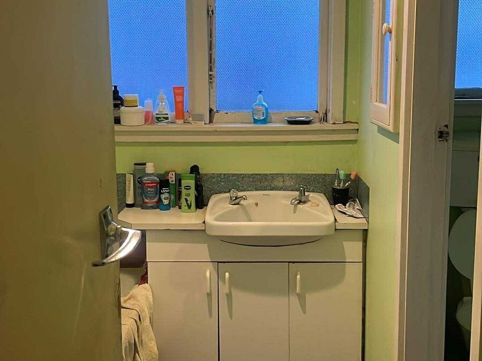 Before: an older bathroom with green walls, a small white vanity under the window and a worn vinyl floor