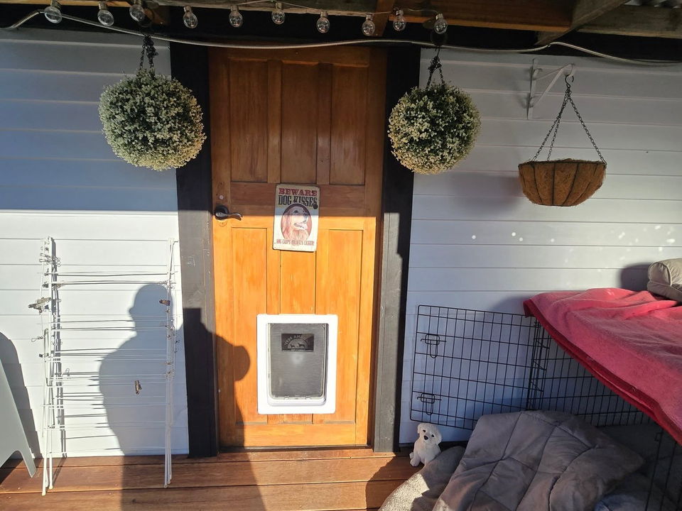 Covered timber deck under a corrugated iron roof, with hanging planters and a pet door in the back door