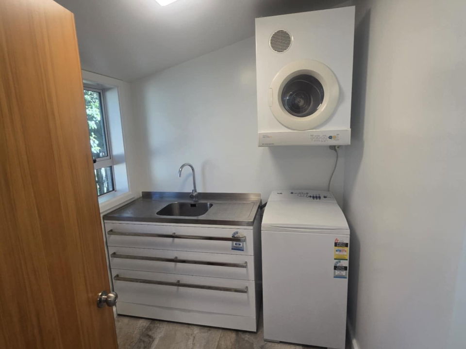 Compact laundry with a wall-mounted dryer above the washing machine, a stainless tub and drawers, and a large-format tiled floor