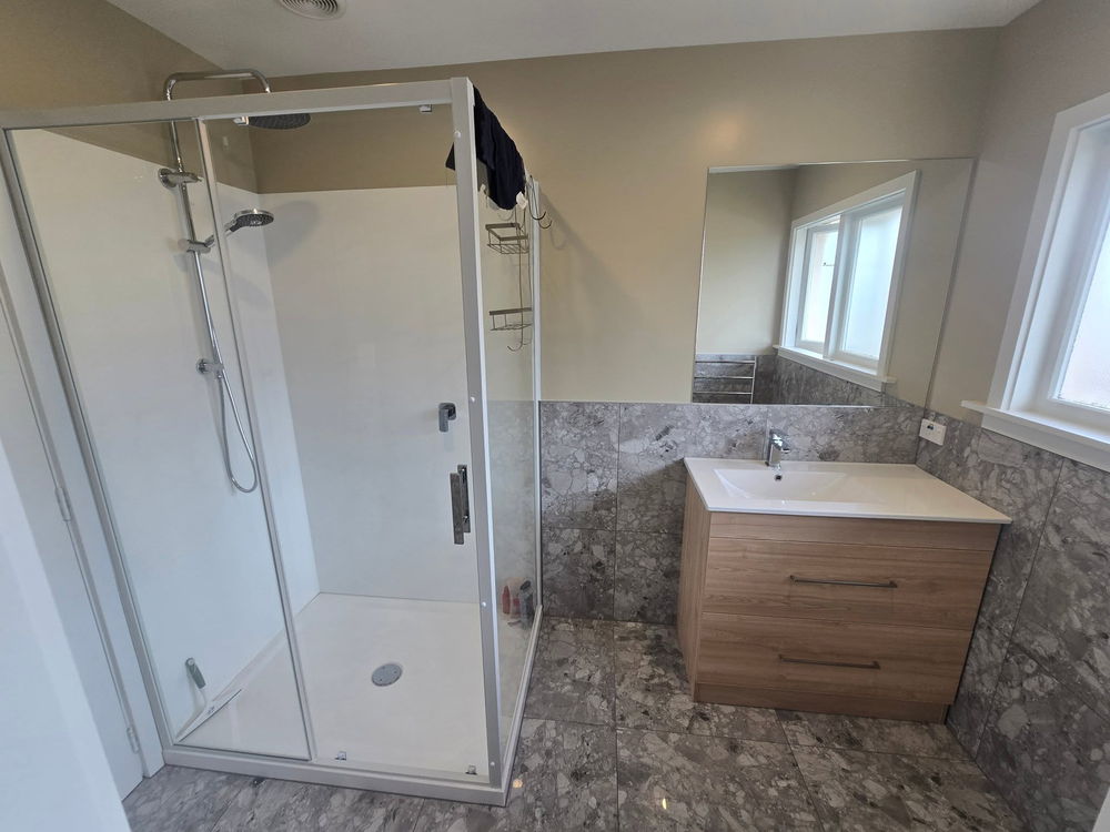 Renovated bathroom with grey stone-look tiles, a glass shower and a timber-look vanity