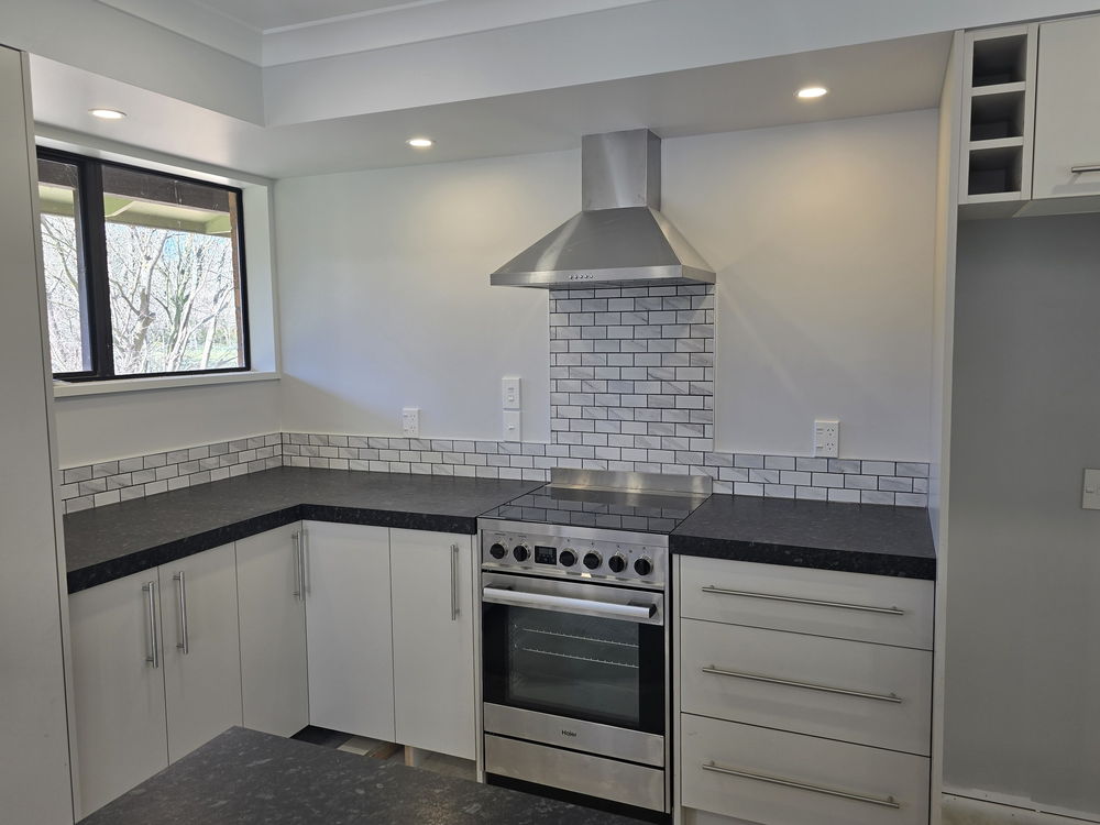 Corner of the new kitchen: ceramic cooktop and stainless rangehood under the marble-look subway tiles, drawers with bar handles, a window onto bare trees
