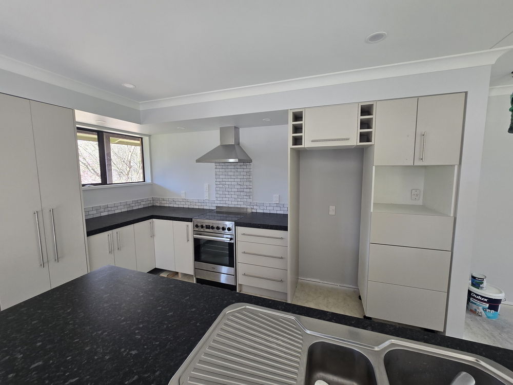 New kitchen with off-white flat-panel cabinetry, a black speckled benchtop, a marble-look subway tile splashback, a stainless rangehood and a freestanding oven