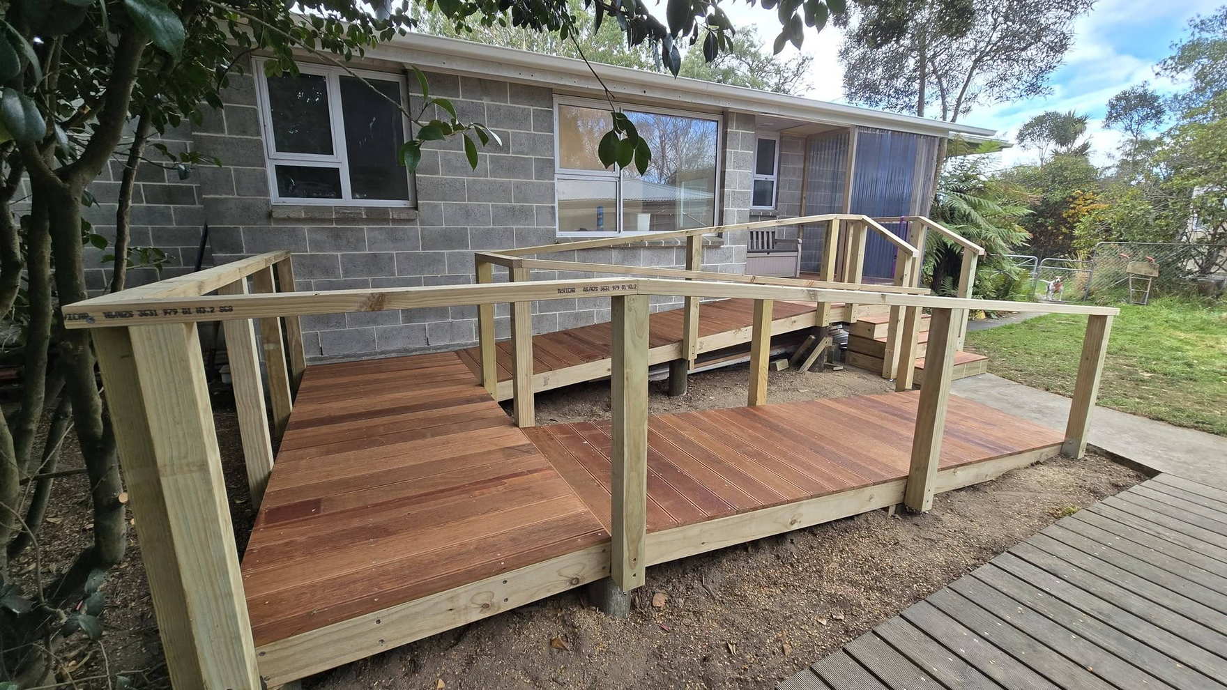 Freshly built timber deck with a post-and-rail balustrade beside a concrete block house, the decking still bright