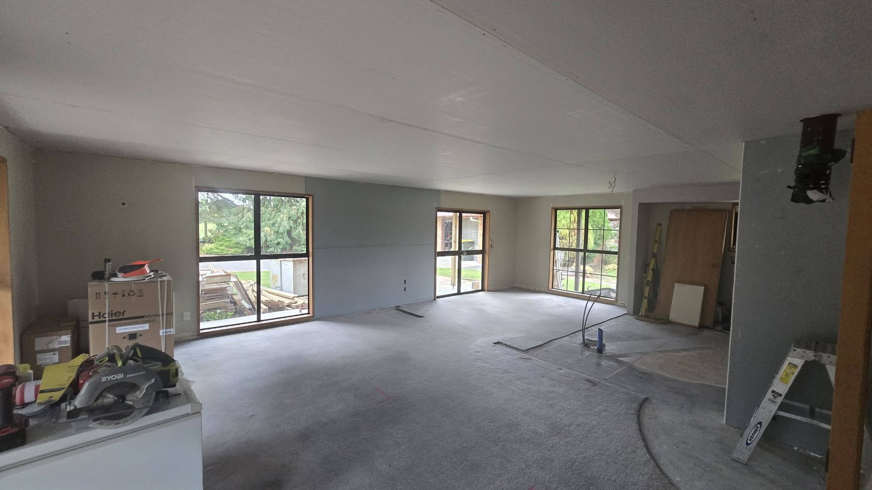 Open-plan living area newly lined with plasterboard, stopped and ready for paint, with windows on two sides