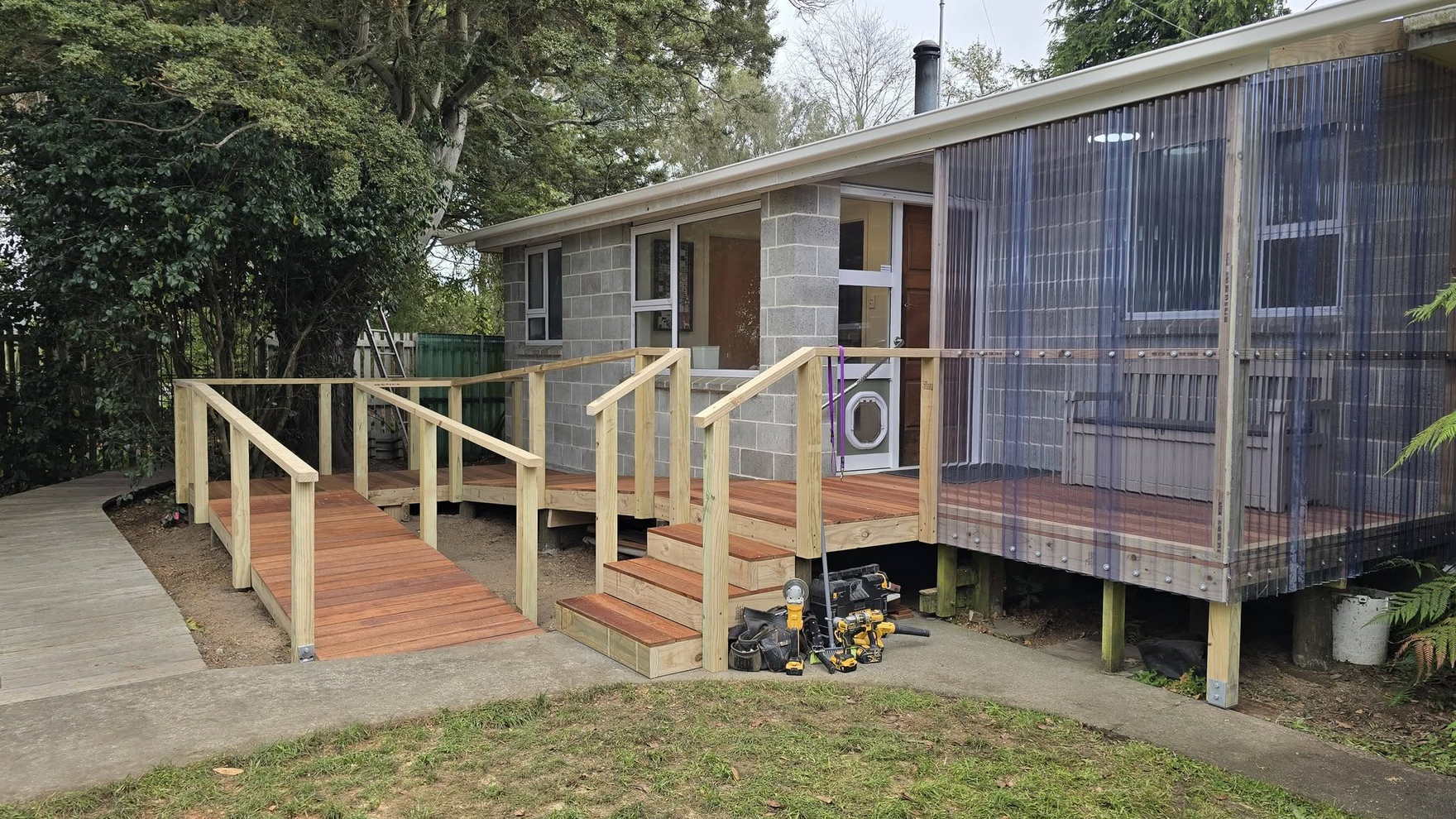 New timber deck with a handrail and an access ramp built onto the back of a concrete block house, lawn in front